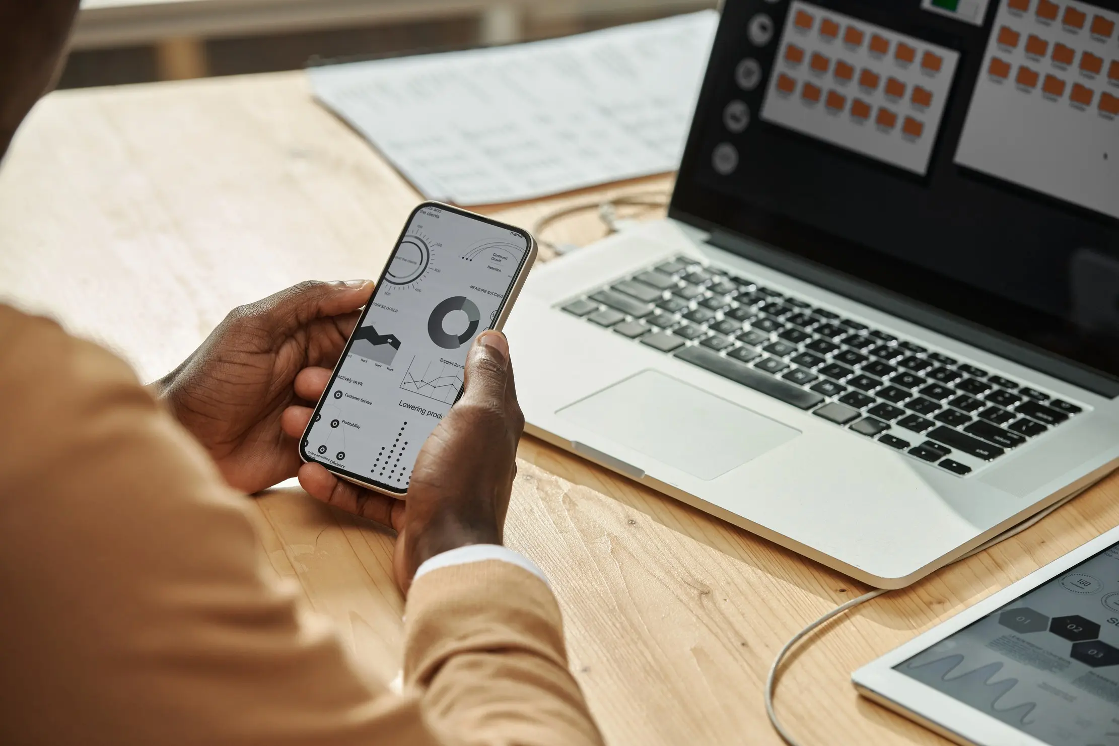 Business manager reviewing sales figures on a phone beside a laptop