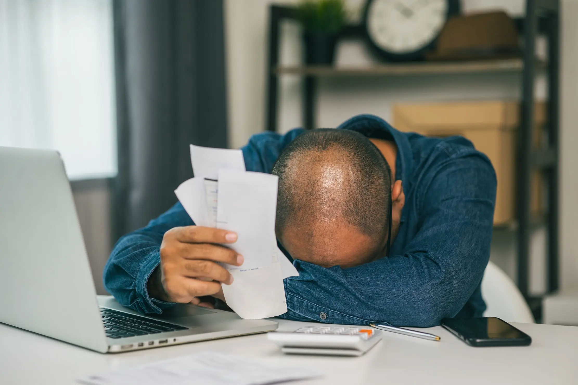 Business customer reviewing unpaid bills beside a laptop during an overdue-payment follow-up