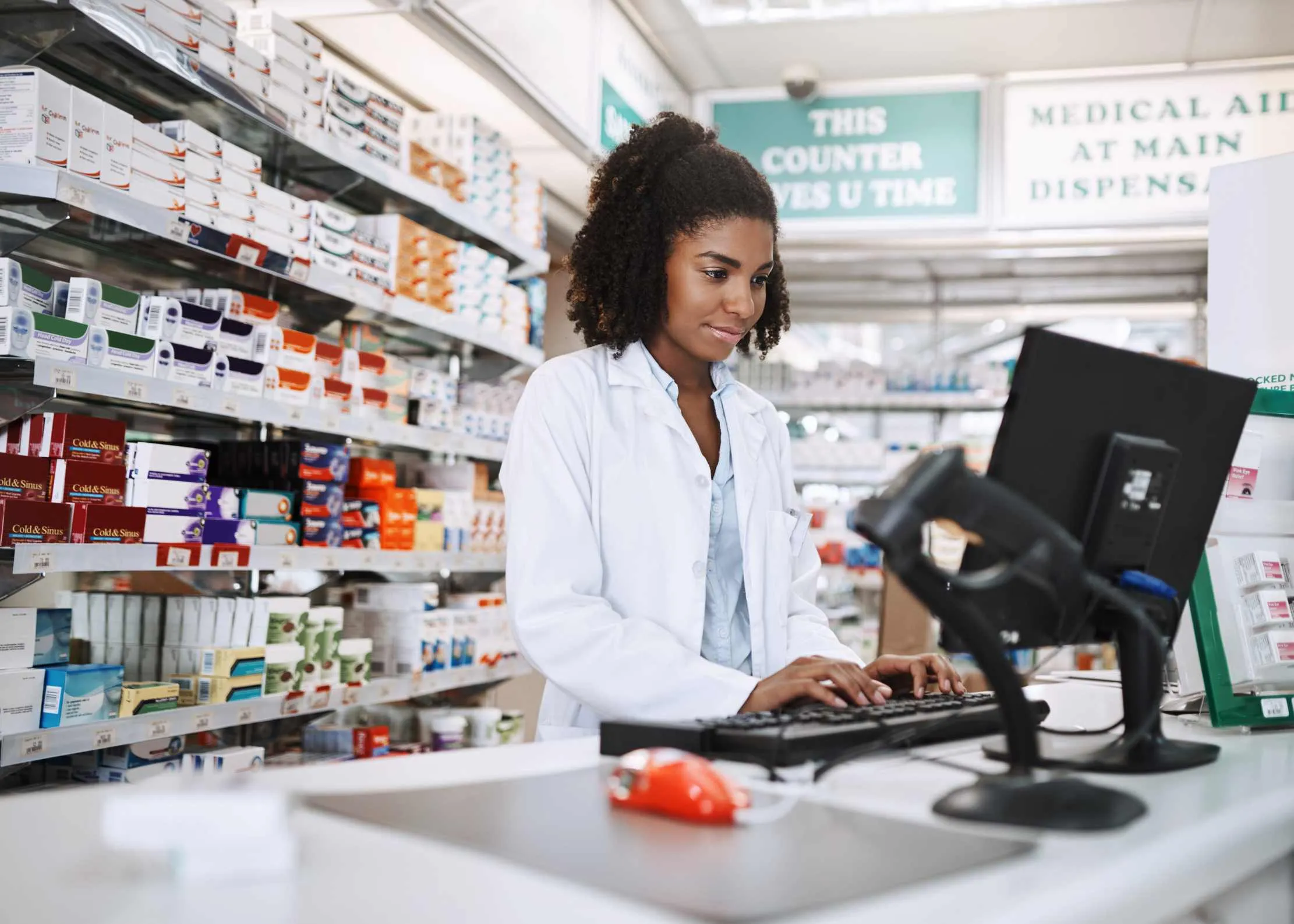 Drug store employee using a computer to manage pharmacy inventory, near-expiry stock, and reorder decisions