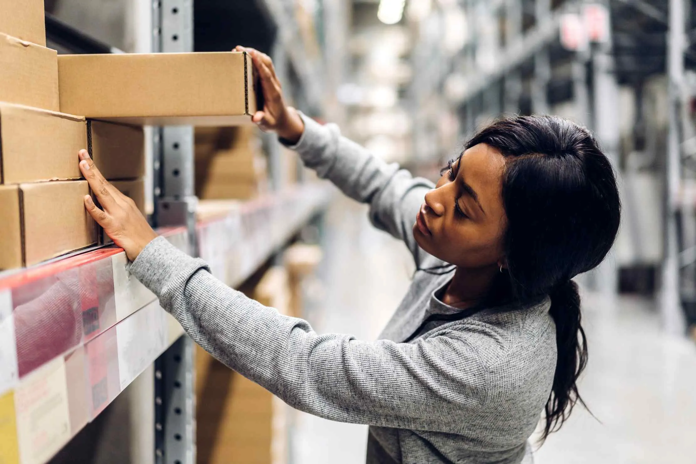 Business owner reviewing inventory and order details beside organised warehouse shelves