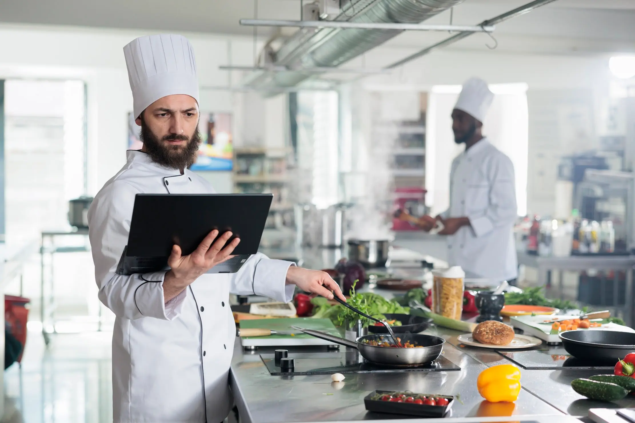 Chef checking a recipe on a laptop while cooking in a professional kitchen