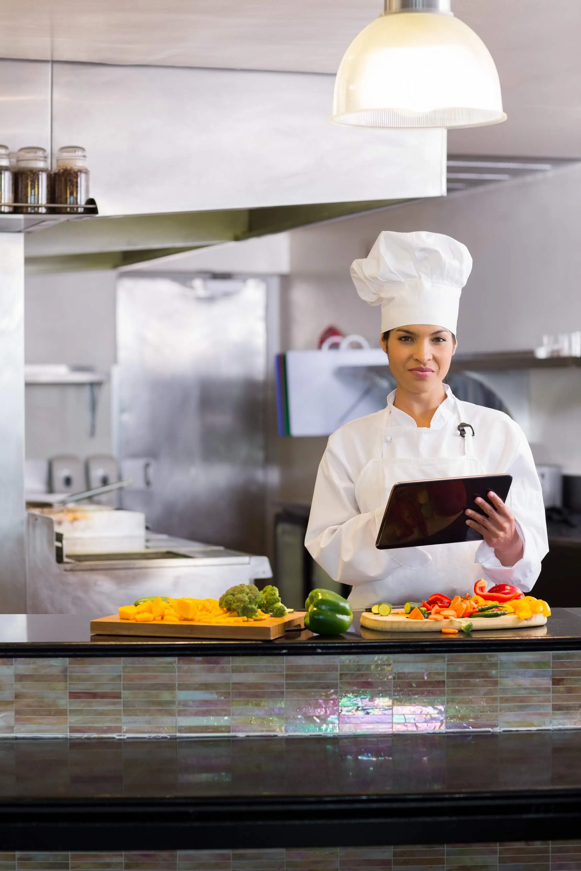 Chef holding a tablet beside prepared vegetables in a professional kitchen